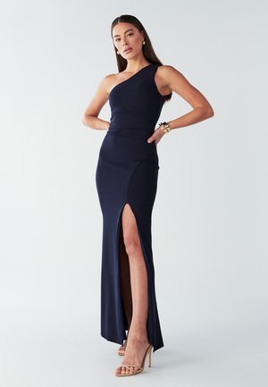 Tumši zila, vienpusējas piegriezuma kleita ar pieguļošu augšu, sānu šķirtni un gludu tekstūru. Apvienota ar ķermeņa krāsas siksnām papēžiem.