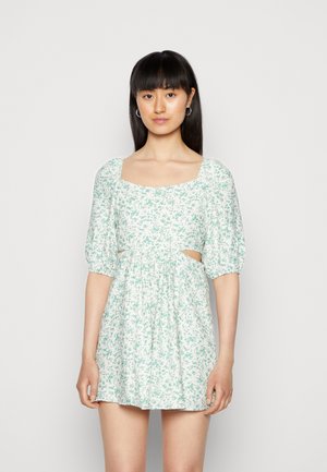 Vestido floral curto em verde claro e branco, apresentando mangas bufantes, decote quadrado, detalhes recortados e uma cintura franzida.