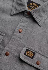 Grau Baumwollhemd mit Button-Down-Kragen, braunen Knöpfen, zwei Brusttaschen und einem Etikett mit "Superdry"-Markenkennzeichnung. Texturiertes Material.