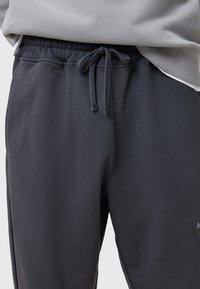Donkergrijze sweatpants van zacht materiaal, voorzien van een elastische tailleband met trekkoord en zijzakken. Minimale branding op het been.