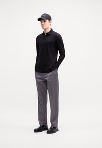 Black long-sleeve polo shirt with a subtle logo on the chest, paired with gray pants and black leather shoes, topped with a black cap.