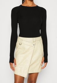 Haut noir à manches longues côtelées associé à une jupe portefeuille en similicuir beige clair avec une texture craquelée, des passants de ceinture et une fermeture par bouton.