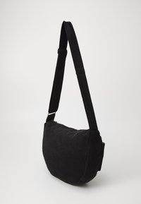 Black corduroy shoulder bag with a padded body, adjustable strap, and zipper closure. Features a curved shape and soft texture.