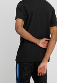 Černé bavlněné tričko s krátkým rukávem, volný střih a kulatým výstřihem, v kombinaci s kalhotami s jemným pruhováním a modrými postranními pruhy.