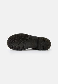 Sola de bota de borracha preta com padrão de ranhura profundo, superfície texturizada e logótipos da marca. Forma curva com bordas definidas para tração e durabilidade.