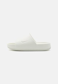 Hvit gummiknotte sandal med en glatt overflate, bred toppstropp og teksturert såle med en subtil Nike-logo.
