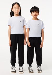 Helllila Kurzarm-T-Shirts mit grünem Logo, kombiniert mit schwarzen schmal geschnittenen Jogginghosen und grauen Sneakers. Einfaches und lässiges Design.