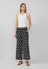 Pantalons larges noirs à pois blancs, taille élastique et poches latérales. Associés à un haut sans manches blanc et des sandales.