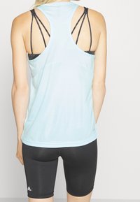 Jasnoniebieska sportowa koszulka bez rękawów z siateczkowymi akcentami, z czarnymi paskami z tyłu, w zestawie z czarnymi dopasowanymi szortami.