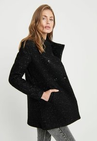 Manteau en mélange de laine noir avec une finition texturée, design double boutonnage, grandes boutons noirs et poches latérales. Manches longues et larges revers.
