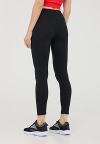 Czarne legginsy o dopasowanym kroju, gładka faktura, z wysokim stanem. Połączone z czarno-szarymi butami sportowymi z fioletowymi akcentami.