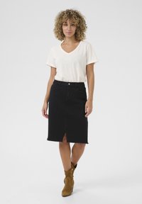 Jupe midi en denim noir avec une fente frontale et un ourlet effiloché, associée à un t-shirt crème à col en V à manches courtes et des bottines marron.