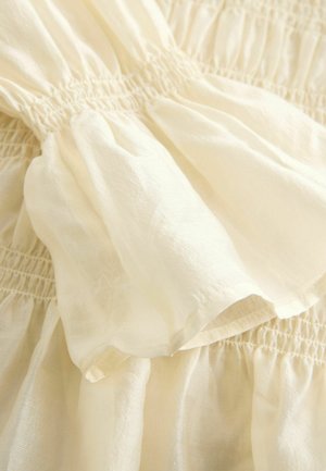 Kreemikarva puuvillane kangas, millel on kogutud osad, pehme ja kerge tekstuur ning elastse vöökohaga detail.