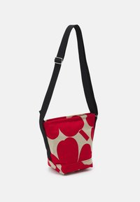 Rød og beige canvas taske med et unikt hjerte mønster, udstyret med en justerbar sort rem og en struktureret, tilspidset form.