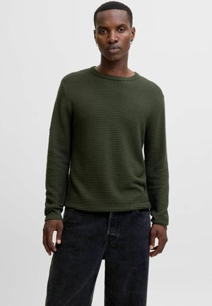 Green ribbed long-sleeve sweater with a crew neck and textured pattern, paired with dark jeans. Features relaxed fit and minimal detailing.