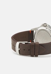 Bracelet de montre en cuir marron avec boucle en argent, arborant une finition texturée et des accents orange. Comprend un détail gravé au dos de la montre.