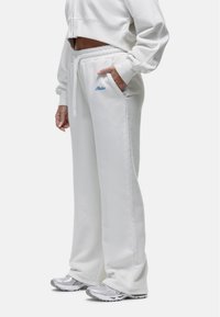 Witte katoenen trainingsoutfit met een elastische tailleband en geborduurde broekspijpen; heeft zijzakken en een blauw geborduurd logo op de linker zak.
