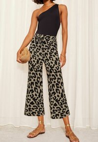 Czarny body na jedno ramię zestawione z oliwkowymi spodniami o szerokich nogawkach w panterkę. Złote sandały na ramiączkach i pleciona torebka dopełniają całość.