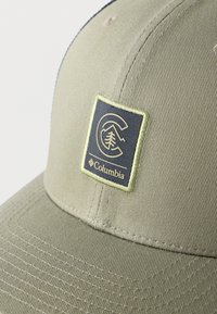 Κοντινό πλάνο σε καπέλο μπέιζμπολ ελιάς με κεντημένη ραφτή μπαλώματα λογότυπου Columbia που απεικονίζει δέντρο και βουνά στο μπροστινό πάνελ.