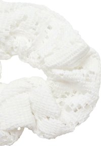 Valkoinen neulekranssi, jossa on teksturoitu kuvio ja avoimia ompeleita, luoden pehmeän ja joustavan muotoilun, joka sopii hiusten kiinnittämiseen.