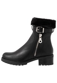 Bottine en cuir noir avec un revers en fausse fourrure, une fermeture éclair latérale et un détail de boucle argentée sur la bride. Elle possède un talon épais et une semelle texturée.