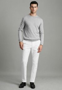 Pulover gri cu mâneci lungi și guler rotund, asortat cu pantaloni albi personalizați și pantofi negri. Linii curate și textură netedă pe tot parcursul.