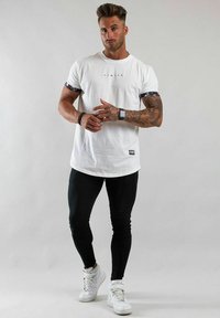 Vit bomull t-shirt med en svart logotyp, mönstrade ärmar, i kombination med svarta leggings och vita högskoor. Helhetsdesign med en figurnära passform.