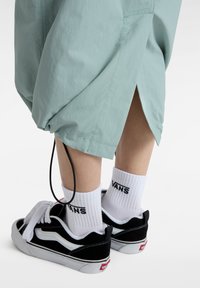 Light green shorts with a tapered design, featuring a drawstring at the hem. Paired with black and white Vans sneakers and white branded socks.