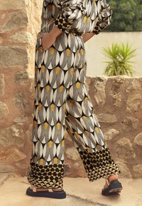 Pantalon à jambes larges avec motif géométrique noir, blanc et or ; fabriqué en tissu léger ; doté de poches et d'une coupe décontractée.