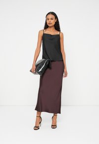 Fekete selyem top, vékony pántokkal, burgundi selyem maxi szoknyával párosítva. A modell egy nagy fekete táskát tart, és szíjakkal ellátott fekete magassarkú cipőt visel.