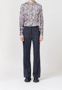 Blouse à manches longues avec un motif floral dans des tons de bleu et d'orange, associée à un pantalon à rayures verticales bleu marine. Des chaussures noires à semelle épaisse complètent le look.