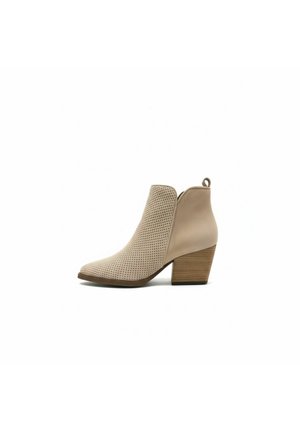 Bota beige hasta el tobillo con parte delantera perforada, parte trasera sólida, tacón bloque de madera y tira para tirar, sobre fondo blanco.