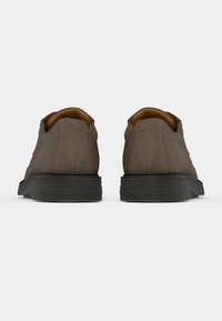 Καφέ σουέτ παπούτσια με κομψό σχέδιο, επίπεδες μαύρες σόλες, αντίθεση ραφών και �στρογγυλή μύτη. Καμία ορατή λογότυπα ή διακοσμήσεις.