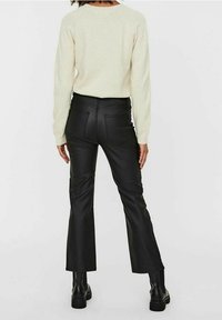 Svarta fusk lädervidbyxor med hög midja, exponerade sömmar och två bakfickor. Stylistiskt kombinerade med en ljusfärgad tröja och svarta stövlar.