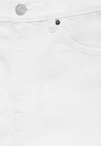 Hvid denimstof med en metalknap, sort nitte og subtilt tekstureret mønster. Inkluderer en frontlomme med synlige sømme.