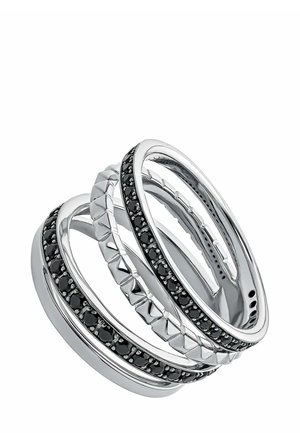 Conjunto de tres anillos entrelazados, de metal plateado, con acentos de gema negra y un patrón geométrico texturizado en una de las bandas.