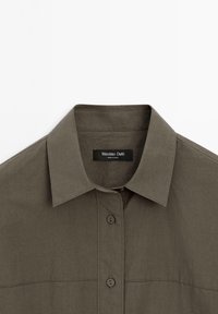 Olive green button-up shirt with a spread collar, featuring a smooth cotton texture and subtle stitching details. Label reads "Massimo Dutti."