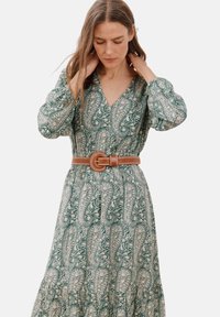 Grünes langes Kleid mit Paisleymuster, V-Ausschnitt, luftigen Ärmeln und einem braunen Gürtel in der Taille. Der Stoff hat eine glatte Textur.