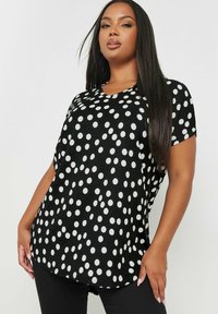 Top nero con pois bianchi, maniche corte, scollatura a cuore, tessuto morbido, orlo arrotondato e vestibilità comoda.