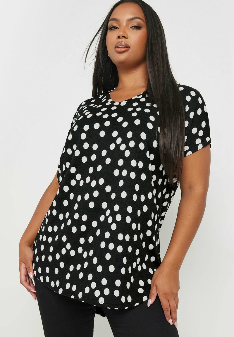 Top nero con pois bianchi, maniche corte, scollatura a cuore, tessuto morbido, orlo arrotondato e vestibilità comoda.