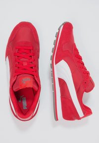 Baskets de sport rouges en suède et en maille, avec une bande latérale blanche, une semelle extérieure grise et des lacets rouges. Logo de la marque visible sur la languette.