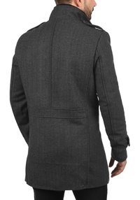 Grijze jas met pied-de-poule patroon, hoge kraag, gestructureerde stof en knoopaccenten. Getailleerde pasvorm met achterventilatiedetail, gezien van achteren.