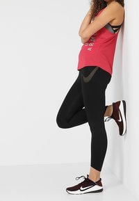 Rotes sportliches Tanktop mit metallischem Schriftzug, schwarze Leggings und weinrote Sneaker mit weißen Akzenten. Strukturiertes, körperbetontes Design.