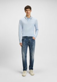 Polo shirt a maniche lunghe di colore azzurro chiaro con colletto a coste bianco e nero, abbinato a jeans blu sbiaditi e sneakers beige.