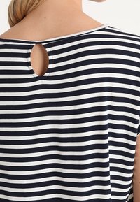 Top a rayas en azul marino y blanco con escote redondo y detalle de ojal en la parte posterior. Material suave, corte holgado, mangas cortas.