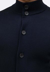 Cardigan di un blu scuro con colletto alto e cinque bottoni neri. Tessuto a maglia текстurizzato con un design aderente.