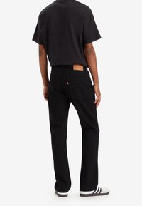 Vaqueros negros de mezclilla con un corte recto, parche de cuero en la parte trasera y dos bolsillos traseros. Combinados con una camiseta negra y zapatillas blancas.