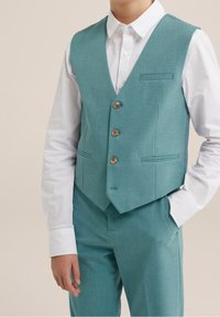 Tyrkysová látková vesta s pěti knoflíky, dvěma kapsami a vykrojenými klopami, spojená s bílou košilí s dlouhým rukávem. Přiléhavý střih.