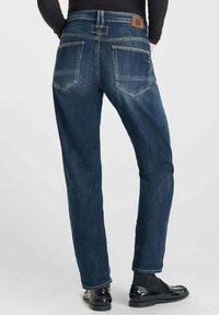 Jeans de mezclilla azul oscuro con un corte recto, dos bolsillos traseros y una pequeña etiqueta de cuero marrón en la cintura.