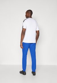 Balts īsās piedurknes krekls ar melniem akcentiem, apvienots ar zilām sporta biksēm un melniem apaviem. Vienkāršs dizains ar brīvu piegriezumu.